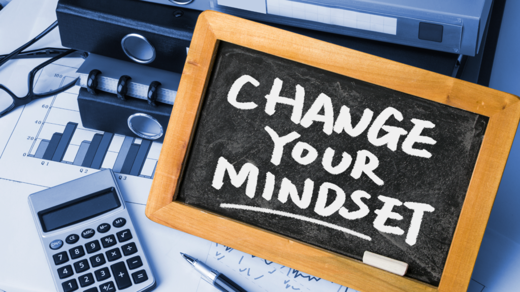 Sign saying Change Your Mindset sitting on top of charts and graphs.