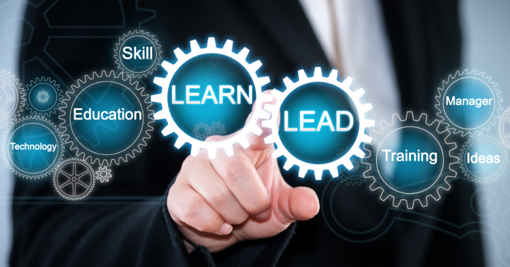 A hand pointing at gears with the words lead and learn on them. Other gears have the words skill, training, education, manager, ideas, and technology on them.