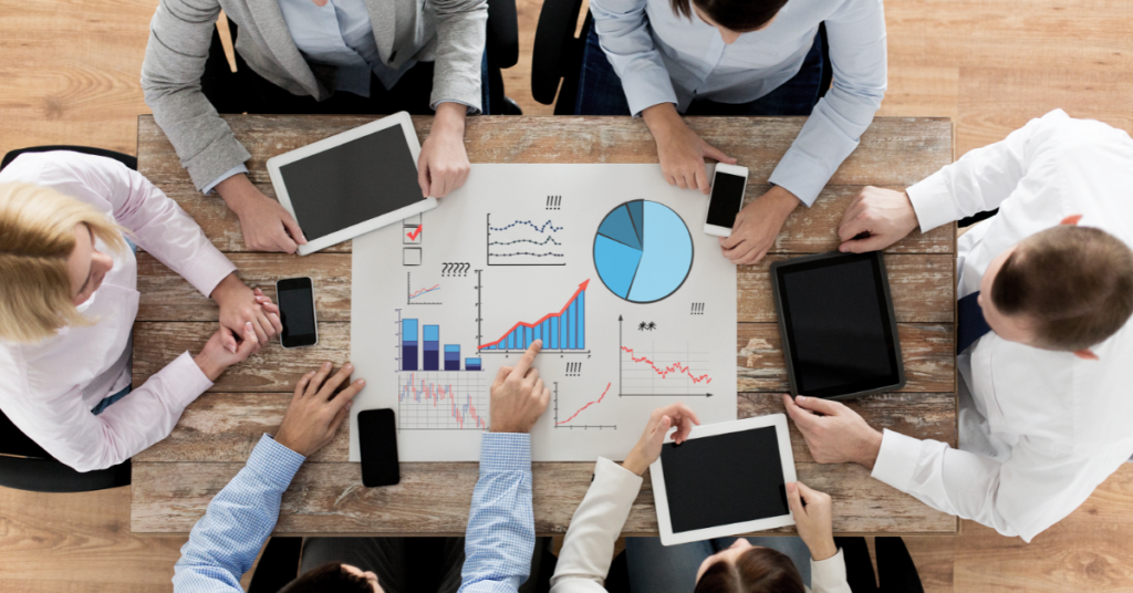 Winning with organization-wide analytics training. Employees working over a table filled with analytics charts and graphs.